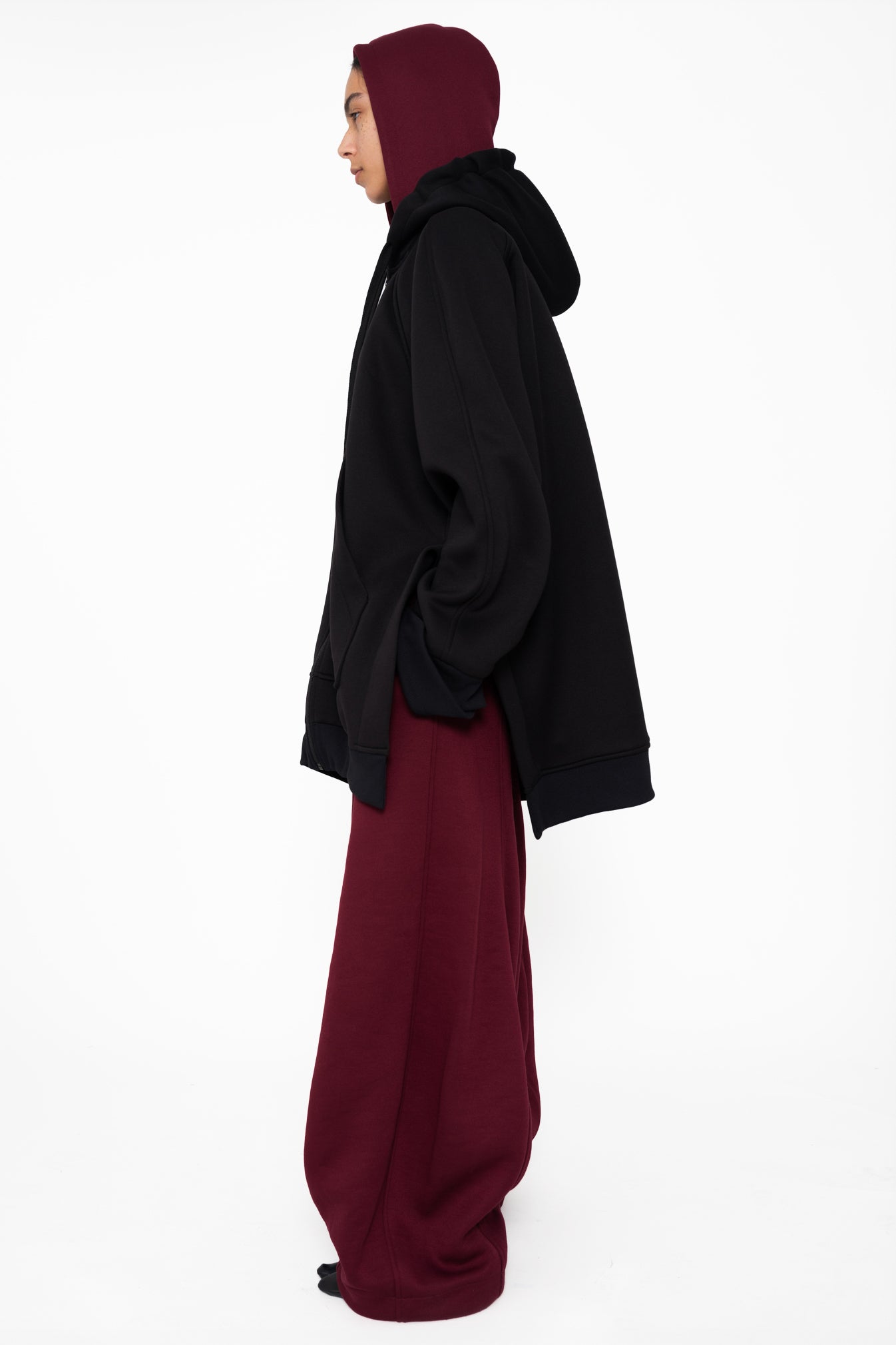 female-wearing-black-oversized-zip-up-hoodie-with-double-hood-in-black-and-bordeaux-on-white-background-fullbody-side