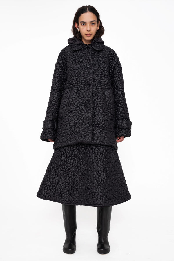 female-wearing-black-quilted-windbreaker-and-black-quilted-midi-skirt-with-flower-embroidery-full-body