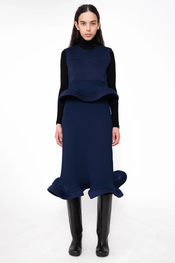 female-wearing-navy-midi-rib-skirt-with-wavy-hem-and-sleeveless-top-with-wavy-hem-and-black-underlayer-on-white-background-full-body-front