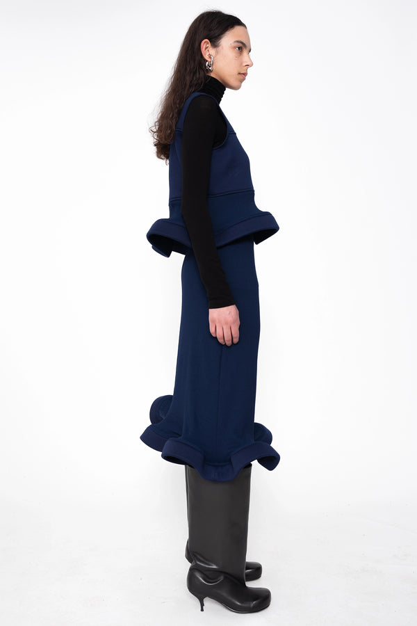 female-wearing-navy-midi-rib-skirt-with-wavy-hem-and-sleeveless-top-with-wavy-hem-and-black-underlayer-on-white-background-full-body-side