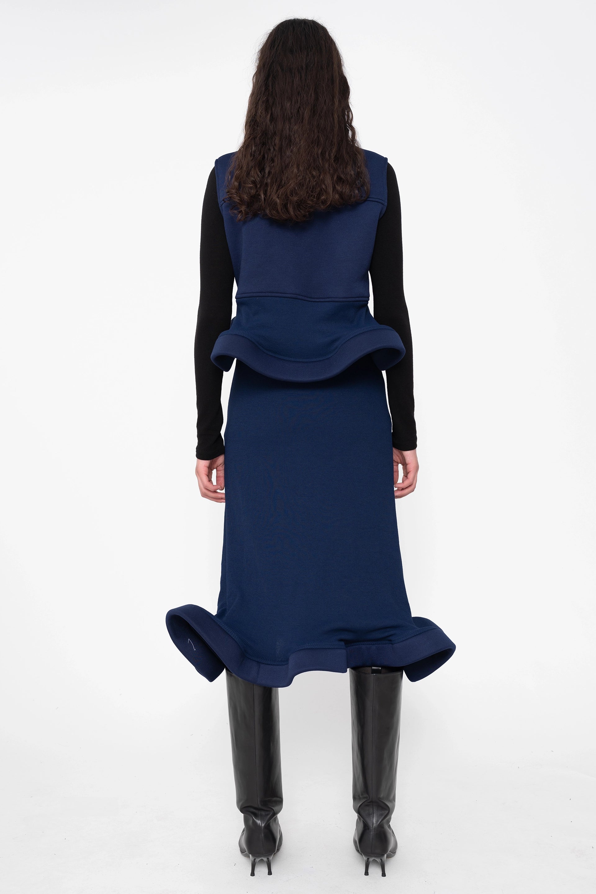 female-wearing-navy-midi-rib-skirt-with-wavy-hem-and-sleeveless-top-with-wavy-hem-and-black-underlayer-on-white-background-full-body-back