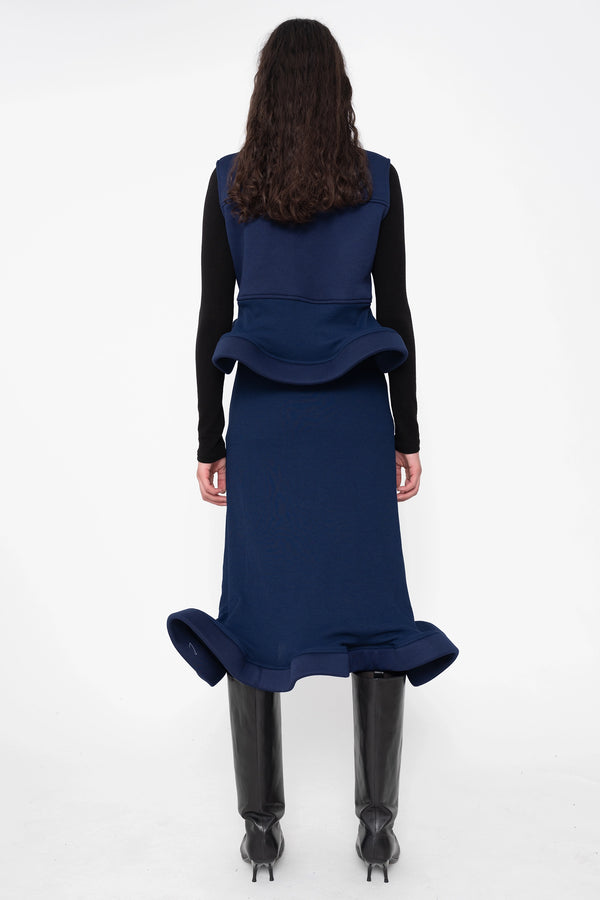 female-wearing-navy-midi-rib-skirt-with-wavy-hem-and-sleeveless-top-with-wavy-hem-and-black-underlayer-on-white-background-full-body-back