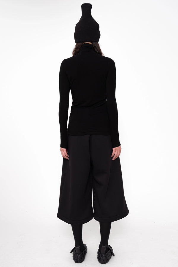 female-wearing-black-turtleneck-and-pierced-beanie-withwide-leg-culottes-on-white-background-full-body-back