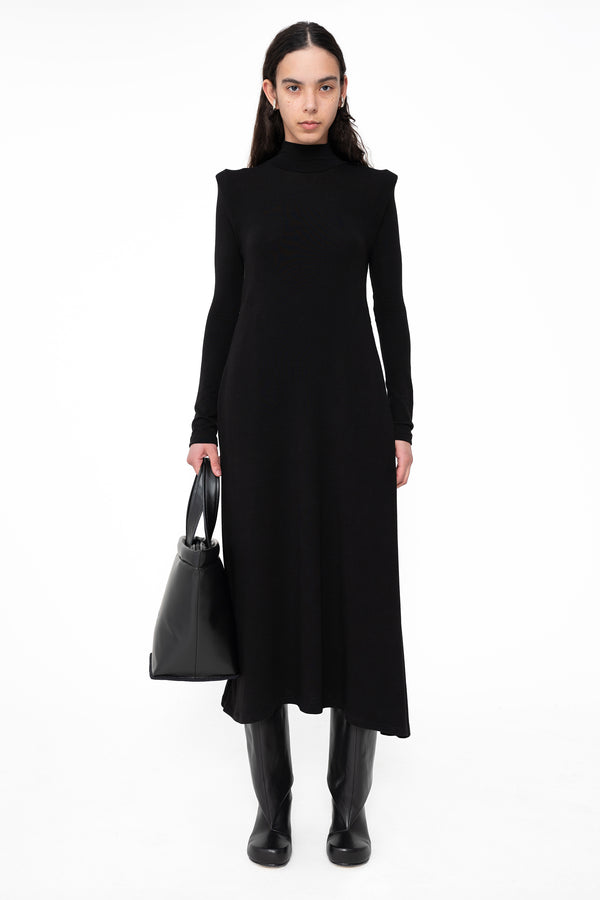 female-wearing-long-black-dress-with-shoulder-detail-and-black-leather-shopper-on-white-background-full-body-front