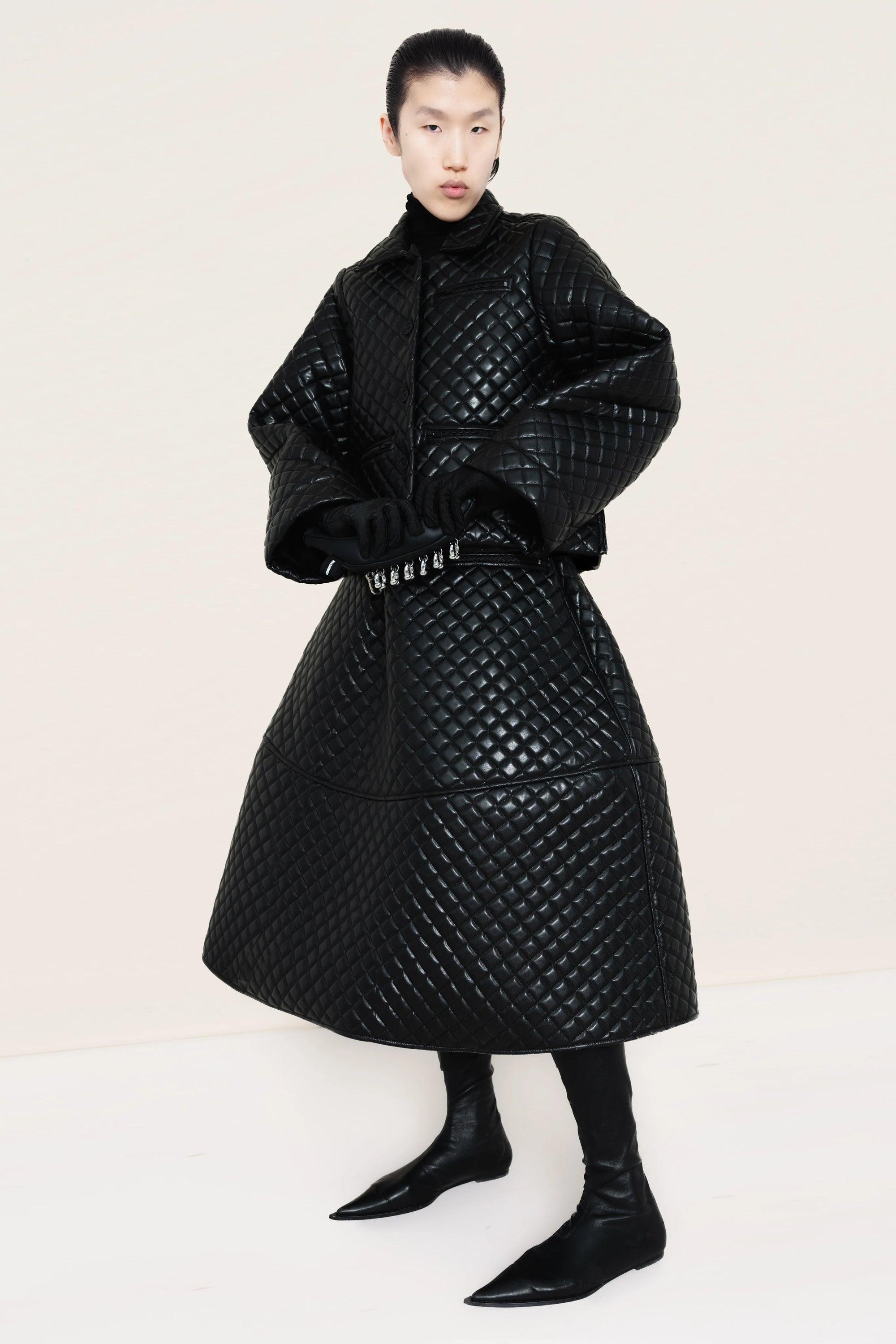 PERSON-WEARING-BLACK-QUILTED-JACKET-AND-SKIRT-HOLDING-BANANA-CLUTCH-WITH-BLACK-POINTY-FLAT-BOOTS