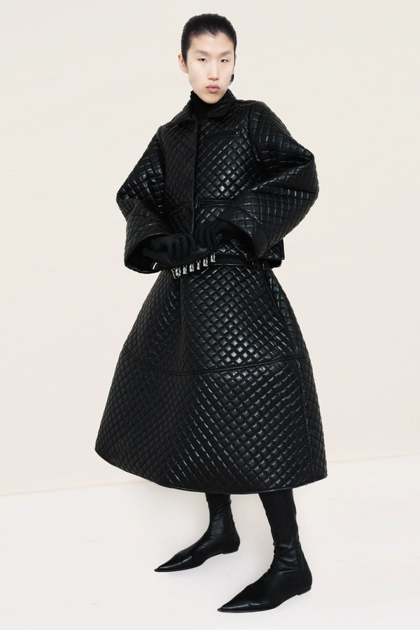 PERSON-WEARING-BLACK-QUILTED-JACKET-AND-SKIRT-HOLDING-BANANA-CLUTCH-WITH-BLACK-POINTY-FLAT-BOOTS