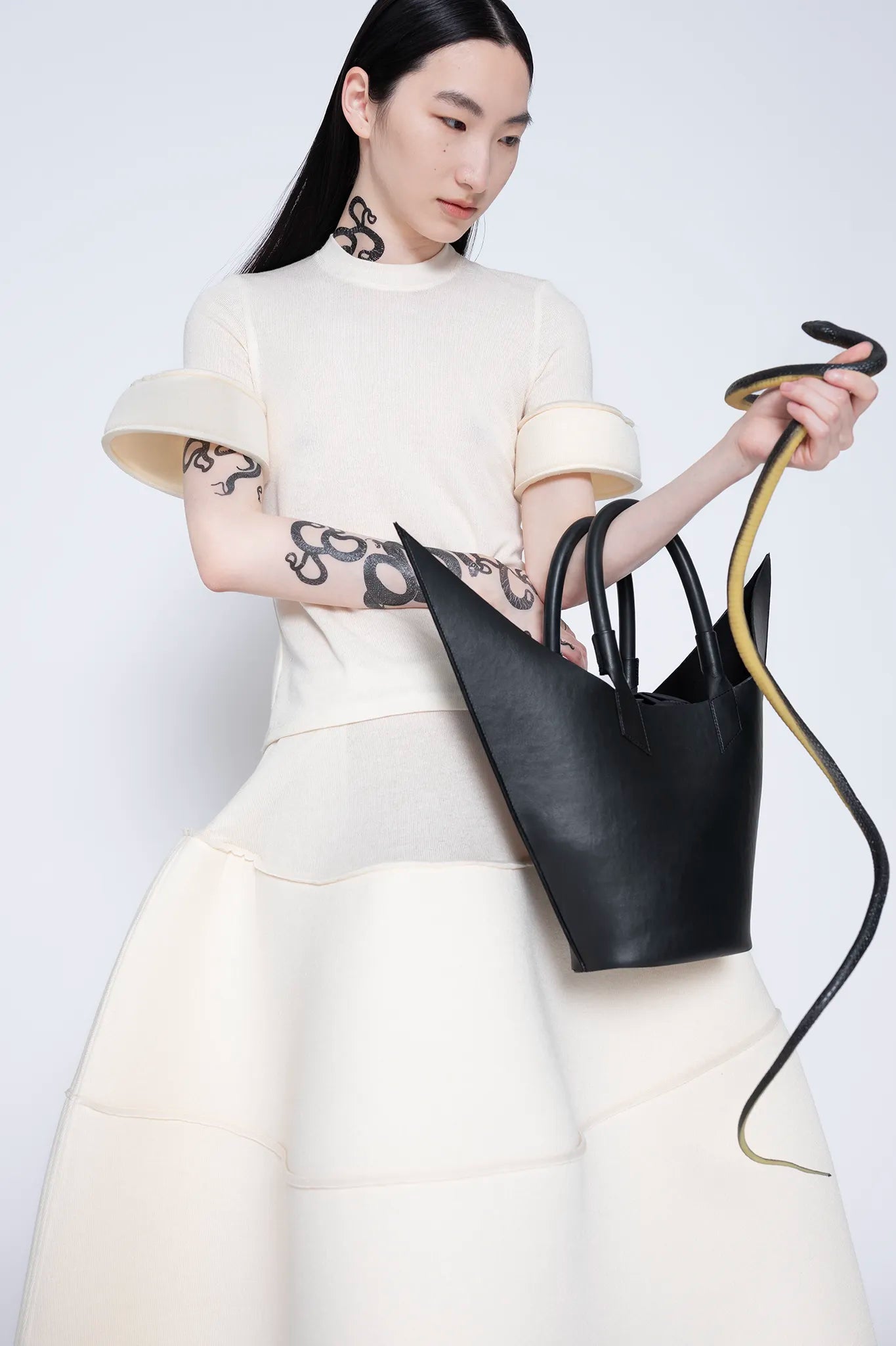 MELITTA-BAUMEISTER-Foam-Cuff-Tee-in-Ivory-UPPER-BODY-FRONT-VIEW-WITH-BLACK-POINTY-SHOULDER-BAG-AND-SNAKE-IN-LEFT-HAND