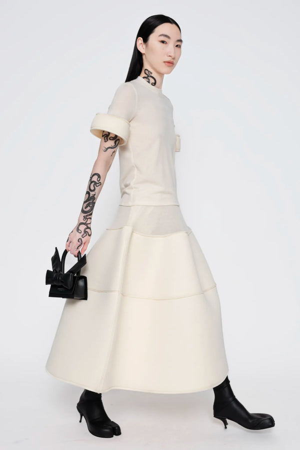 MELITTA-BAUMEISTER-Foam-Cuff-Tee-in-Ivory-FULL-BODY-RIGHT-SIDE-VIEW-FEMALE-IN-MOTION-WITH-SMALL-LEATHER-BOW-BLACK-BAG-IN-RIGHT-HAND