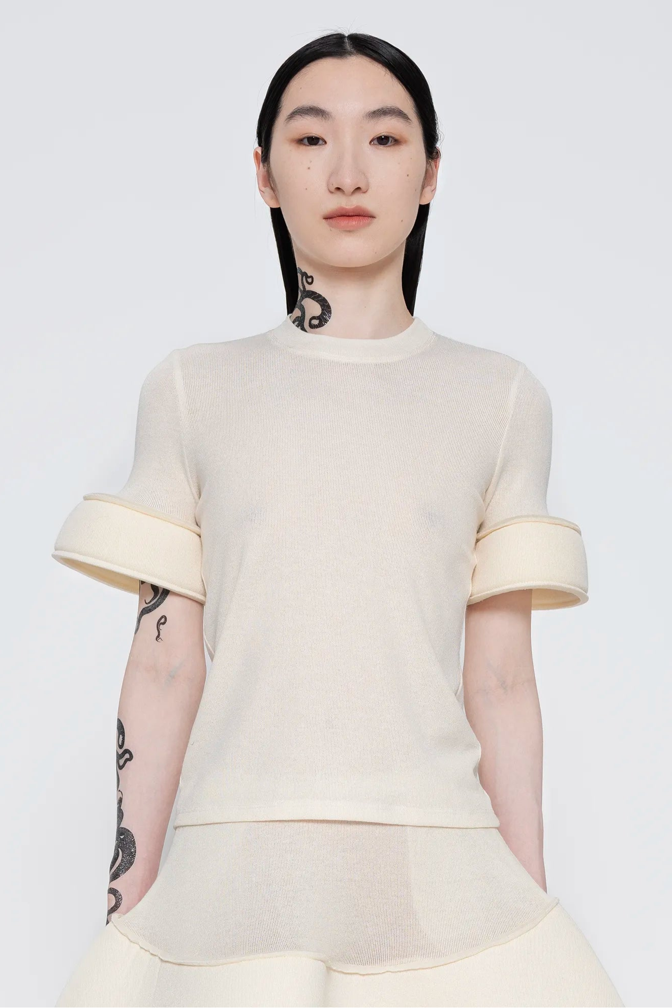 MELITTA-BAUMEISTER-Foam-Cuff-Tee-in-Ivory-UPPER-BODY-VIEW-BLACK-LONG-HAIR-FEMALE-MODEL-WITH-SNAKE-TATTOOS-ON-NECK-AND-RIGHT-ARM