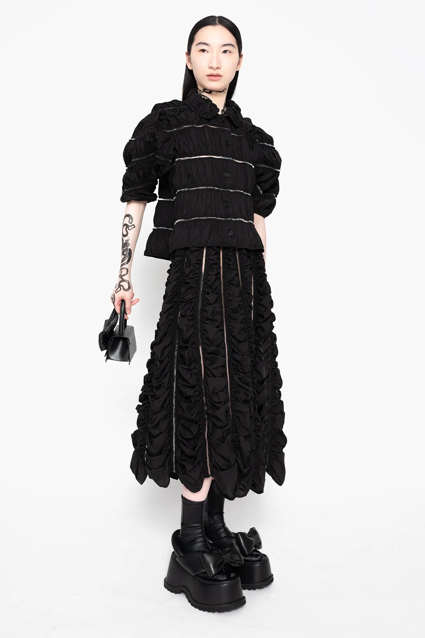 MELITTA-BAUMEISTER-Ruched-A-Line-Skirt-Black-LONG-BLACK-HAIR-FEMALE-MODEL-ALSO-WEARING-SAME-MATERIAL-TOP-AND-BLACK-LEATHER-BOW-SHOES-AND-SMALL-BLACK-LEATHER-HANDBAG-IN-RIGHT-HAND