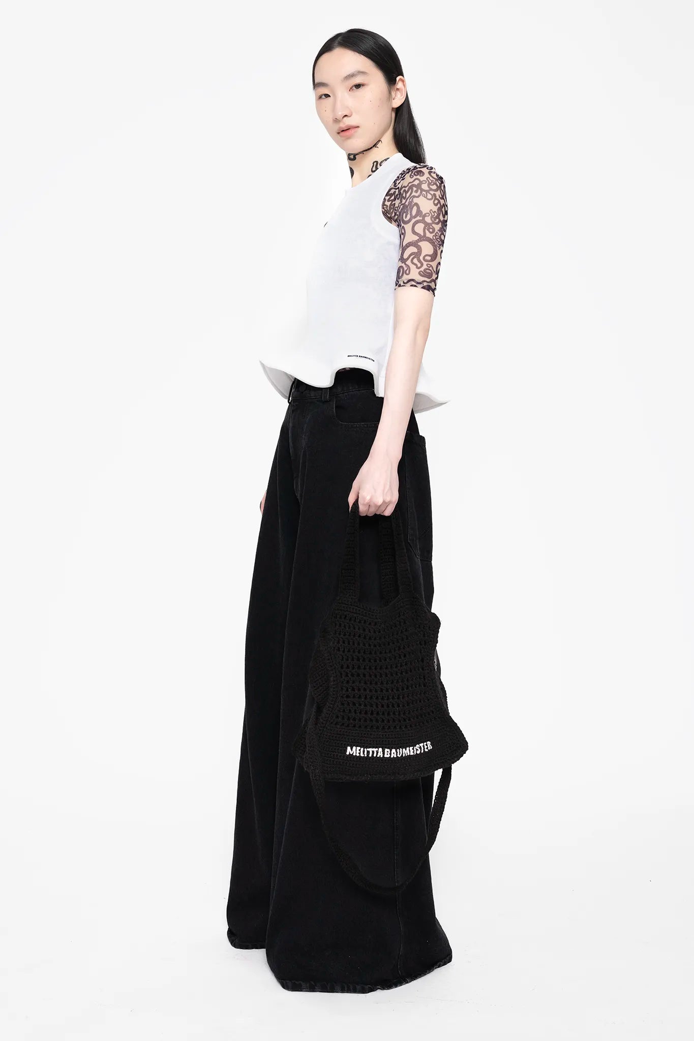 MELITTA-BAUMEISTER-Cropped-Foam-Hem-Tank-SLIGHT-LEFT-SIDE-VIEW-FULL-BODY-MODEL-ALSO-WEARING-BLACK-DENIM-PANTS-AND-HOLDING-BLACK-KNITTED-BAG