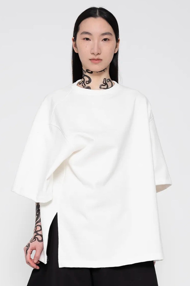 MELITTA-BAUMEISTER-Twisted-Tee-White-LONG-BLACK-HAIR-FEMALE-MODEL-WITH-NECK-AND-ARM-SNAKE-TATTOOS-ALSO-WEARING-OVERSIZED-BLACK-PANTS-AND-BLACK-LEATHER-BOW-SANDALS