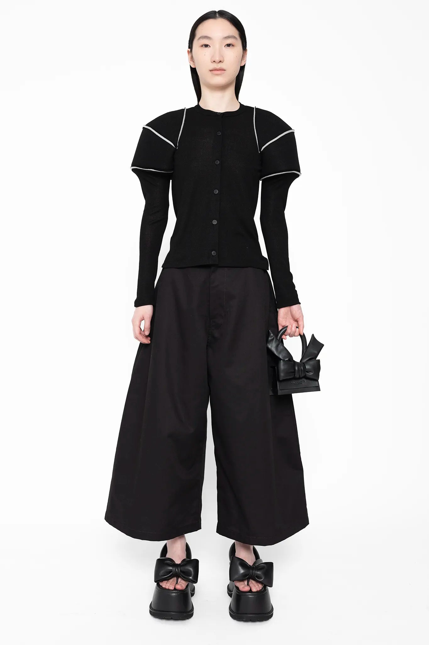 MELITTA-BAUMEISTER-Wide-Leg-Culotte-Black-LONG-BLACK-HAIR-FEMALE-MODEL-ALSO-WEARING-LARGE-SHOULDER-TOP-WITH-WHITE-STRIPES-HOLDING-THE-TINY-LEATHER-BLACK-BOW-BAG-AND-WEARING-BLACK-LEATHER-BOW-SHOES