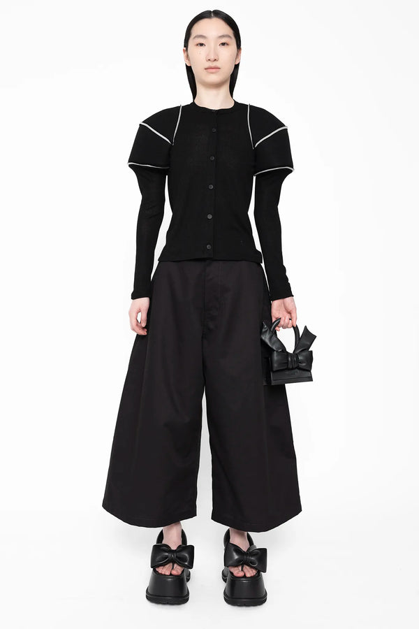 MELITTA-BAUMEISTER-Wide-Leg-Culotte-Black-LONG-BLACK-HAIR-FEMALE-MODEL-ALSO-WEARING-LARGE-SHOULDER-TOP-WITH-WHITE-STRIPES-HOLDING-THE-TINY-LEATHER-BLACK-BOW-BAG-AND-WEARING-BLACK-LEATHER-BOW-SHOES