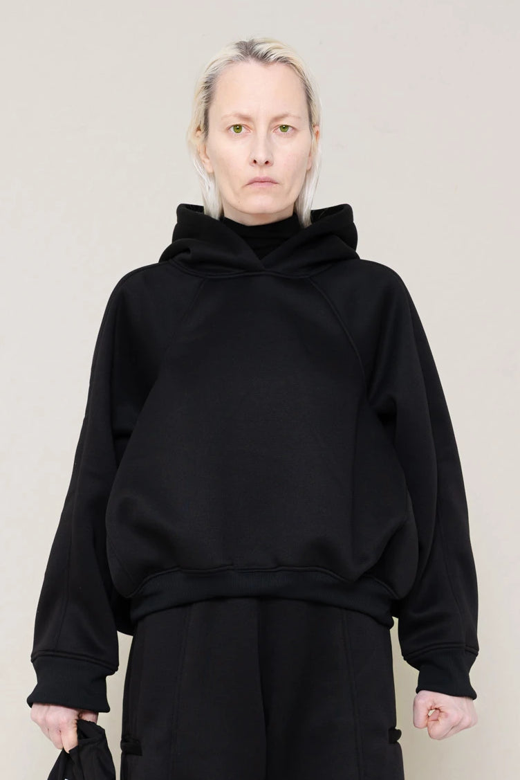 PERSON-WEARING-BLACK-CROPPED-HOODIE-WITH-MATCHING-BLACK-ROUND-LEG-LOUNGEPANTS-AND-BLACK-FLAT-POINTY-BOOTS-HOLDING-PIERCED-BLACK-BANANA-TOTE-BAG-CLOSE-UP-FRONT-VIEW