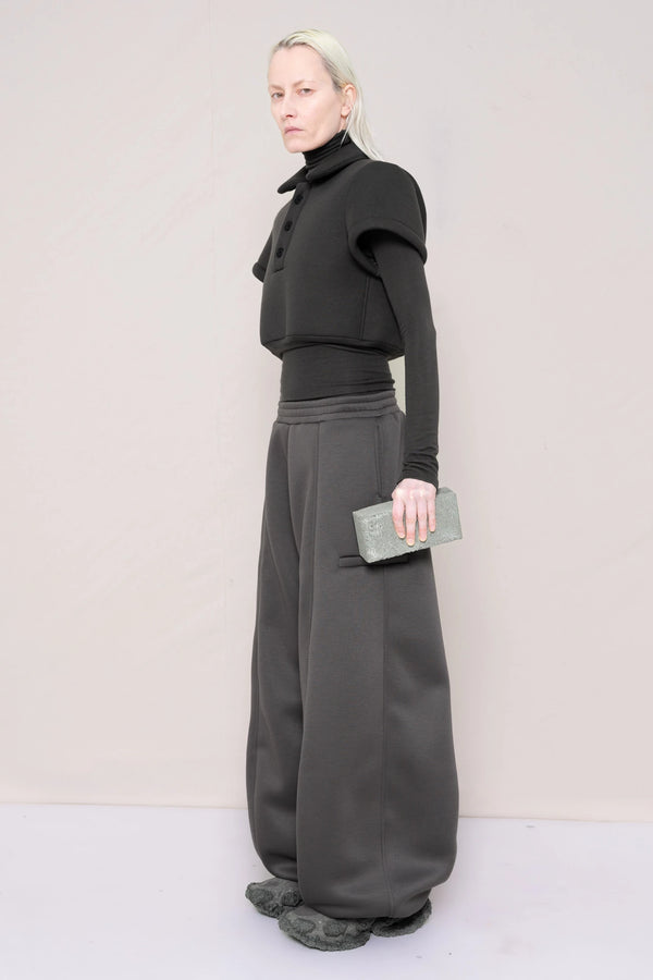 PERSON-WEARING-WARM-GREY-FOAMY-POLO-AND-LONGSLEEVE-TURTLENECK-WITH-STONE-GREY-ROUND-LEG-LOUNGEPANTS-AND-CUSTOMIZED-SNEAKERS-WHILE-HOLDING-GREY-BRICK-THREE-QUARTER-VIEW