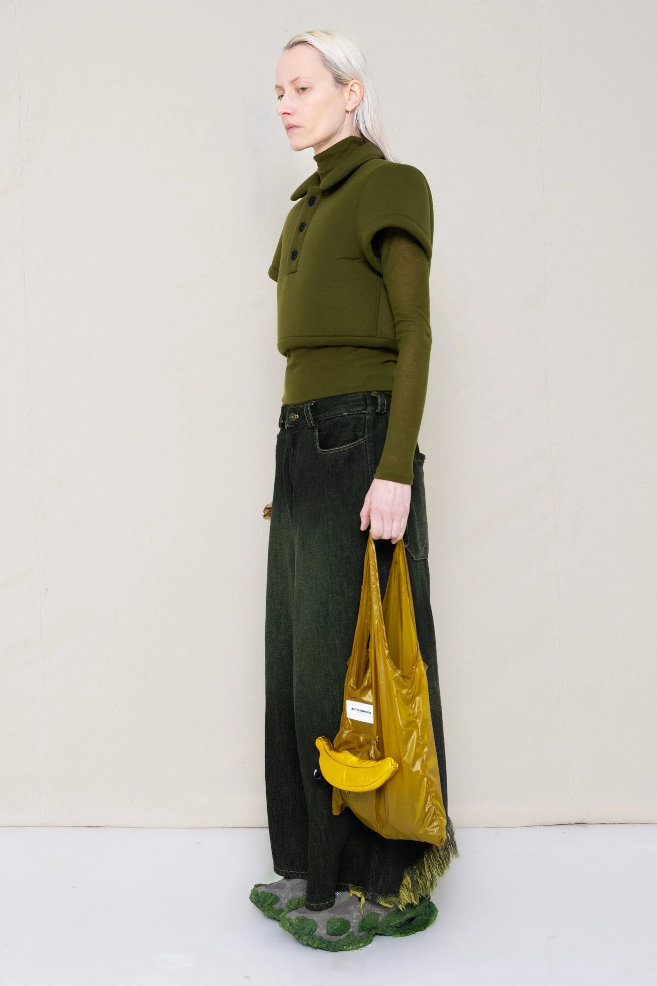PERSON-WEARING-MOSS-FOAMY-POLO-WITH-MOSS-LONG-SLEEVE-TURTLENECK-UNDER-AND-BLACK-YELLOW-WASH-DENIM-PANTS-WITH-CUSTOMIZED-SNEAKERS-HOLDING-GOLD-BANANA-TOTE-BAG-THREE-QUARTER-VIEW