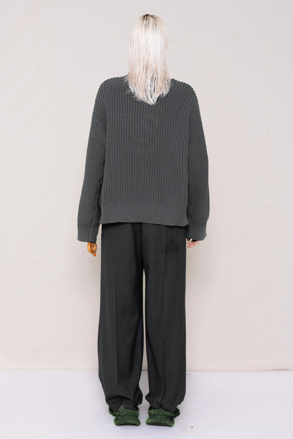 woman-holding-a-pretzel-wearing-a-gray-knit-turtle-neck-sweater-with-a-smiley-face-cut-out-and-grey-WOOL-BLEND-TWILL-TAILORED-PANTS-WITH-ZIGZAG-HEM-DETAIL-worn-with-custom-shoes-full-body-back-view