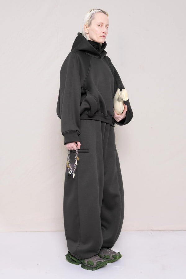 PERSON-WEARING-STONE-GREY-CROPPED-HOODIE-WITH-MATCHING-STONE-GREY-ROUND-LEG-LOUNGEPANTS-HOLDING-MB-CHARM-NECKLACE-AND-HOT-WATER-BOTTLE-WITH-CUSTOMIZED-SNEAKERS-THREE-QUARTER-VIEW