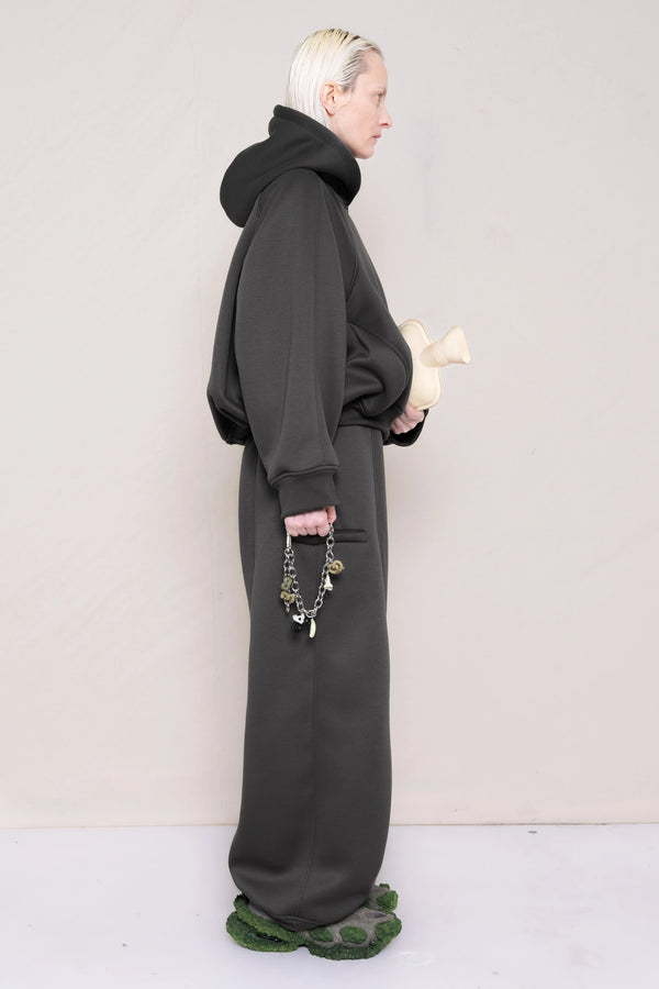 PERSON-WEARING-STONE-GREY-CROPPED-HOODIE-WITH-MATCHING-STONE-GREY-ROUND-LEG-LOUNGEPANTS-HOLDING-MB-CHARM-NECKLACE-AND-HOT-WATER-BOTTLE-WITH-CUSTOMIZED-SNEAKERS-SIDE-VIEW