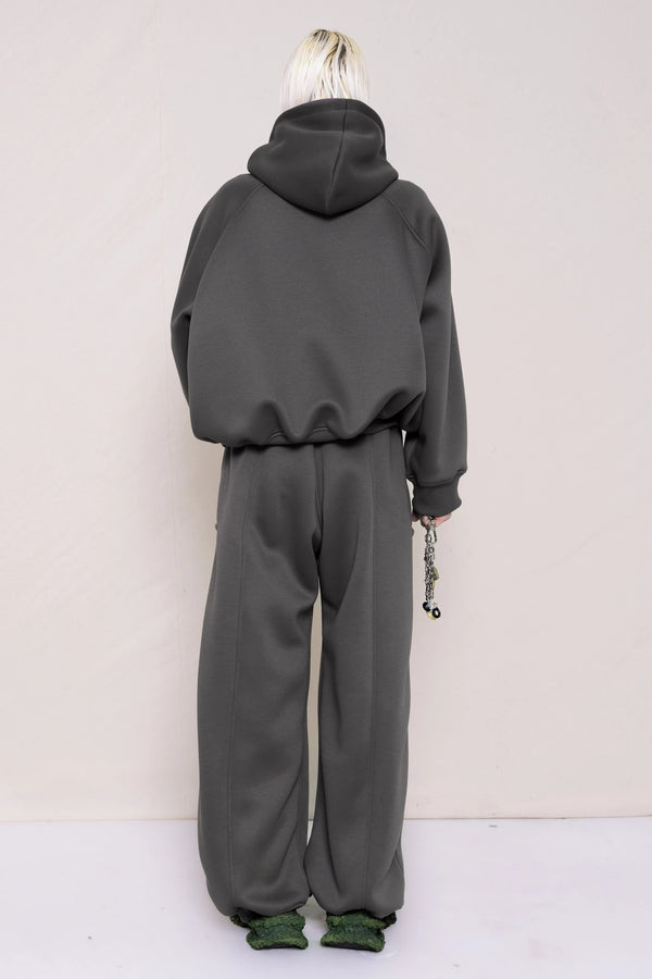 PERSON-WEARING-STONE-GREY-CROPPED-HOODIE-WITH-MATCHING-STONE-GREY-ROUND-LEG-LOUNGEPANTS-HOLDING-MB-CHARM-NECKLACE-AND-HOT-WATER-BOTTLE-WITH-CUSTOMIZED-SNEAKERS-BACK-VIEW