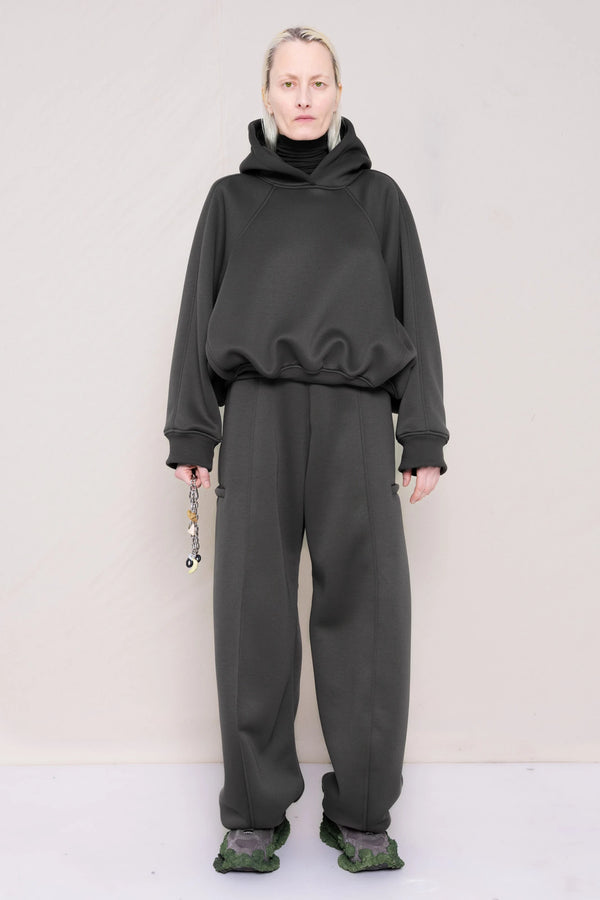 PERSON-WEARING-STONE-GREY-CROPPED-HOODIE-WITH-MATCHING-STONE-GREY-ROUND-LEG-LOUNGEPANTS-HOLDING-MB-CHARM-NECKLACE-WITH-CUSTOMIZED-SNEAKERS-FRONT-VIEW