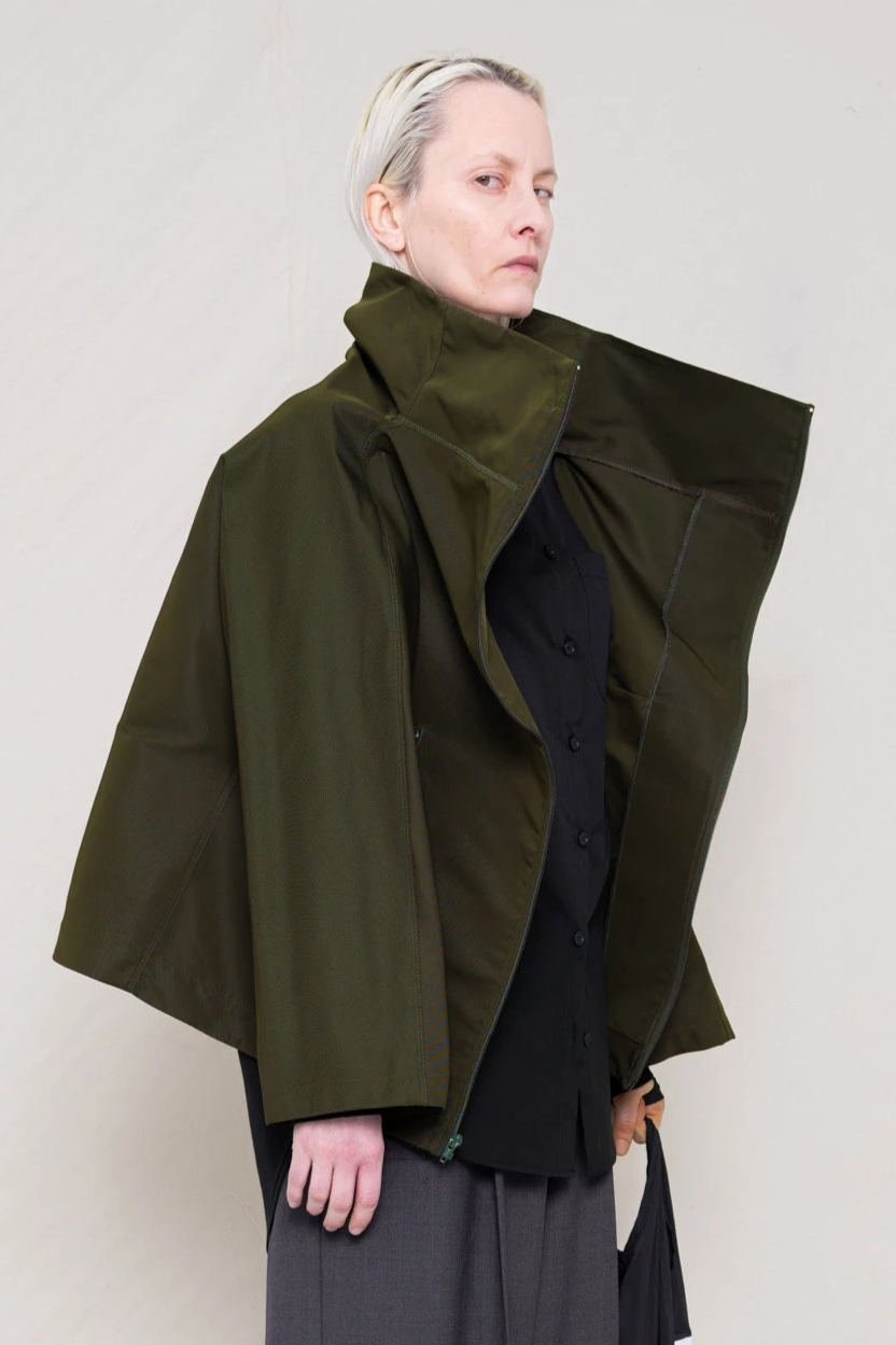 PERSON-WEARING-BLACK-SLIM-SLEEVE-BUTTON-DOWN-UNDER-MOSS-BOXY-ZIP-UP-JACKET-WITH-GREY-TAILORED-PANTS-HOLDING-BAG-CLOSE-UP-THREE-QUARTER-VIEW