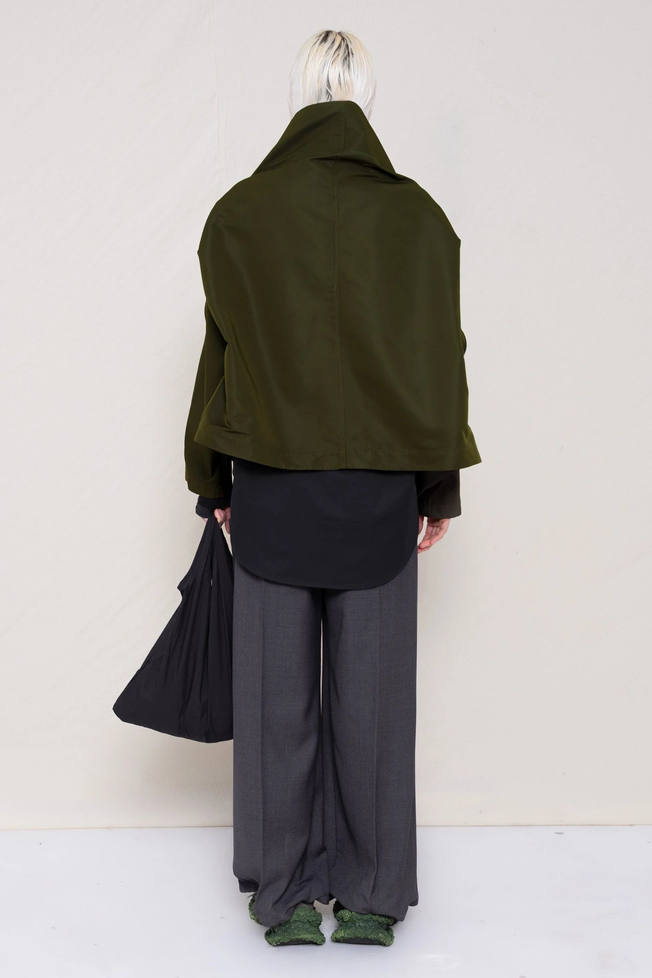 PERSON-WEARING-MOSS-BODY-ZIP-UP-JACKET-WITH-BLACK-BUTTON-DOWN-AND-GREY-TAILORED-PANTS-AND-CUSTOMIZED-SNEAKERS-HOLDING-GREY-BANANA-TOTE-BAG-BACK-VIEW