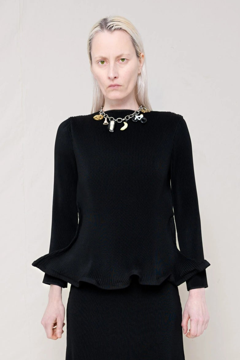 PERSON-WEARING-BLACK-RIPPLE-PLEAT-ZIG-ZAG-HEM-TOP-AND-MATCHING-RIPPLE-PLEAT-ZIG-ZAG-HEM-SKIRT-ACCESSORIZED-MB-CHARM-NECKLACE-CLOSE-UP-FRONT-VIEW
