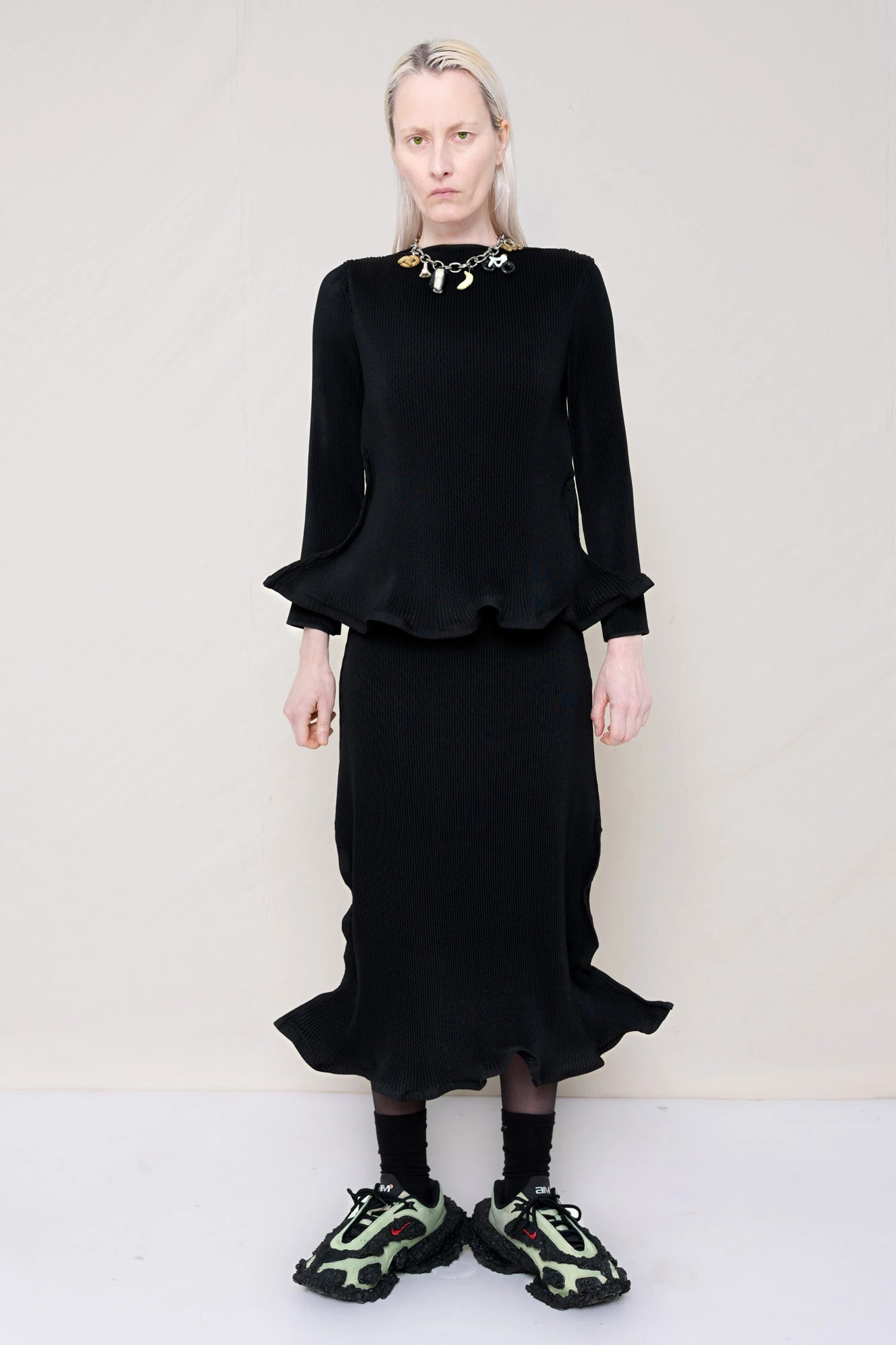PERSON-WEARING-BLACK-RIPPLE-PLEAT-ZIG-ZAG-HEM-TOP-AND-MATCHING-RIPPLE-PLEAT-ZIG-ZAG-HEM-SKIRT-ACCESSORIZED-WITH-CUSTOMIZED-SNEAKERS-AND-MB-CHARM-NECKLACE-FRONT-VIEW