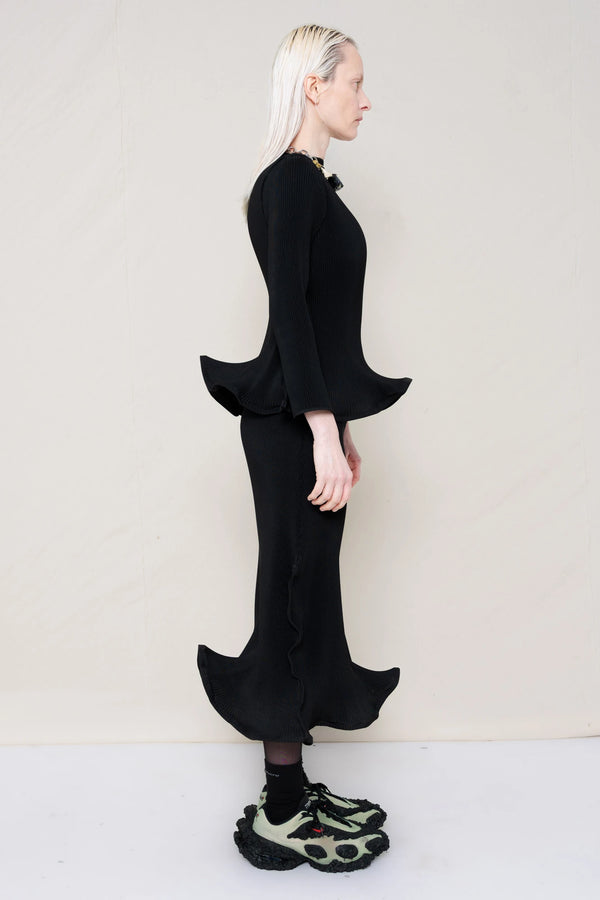 PERSON-WEARING-BLACK-RIPPLE-PLEAT-ZIG-ZAG-HEM-TOP-AND-MATCHING-RIPPLE-PLEAT-ZIG-ZAG-HEM-SKIRT-ACCESSORIZED-WITH-CUSTOMIZED-SNEAKERS-AND-MB-CHARM-NECKLACE-SIDE-VIEW