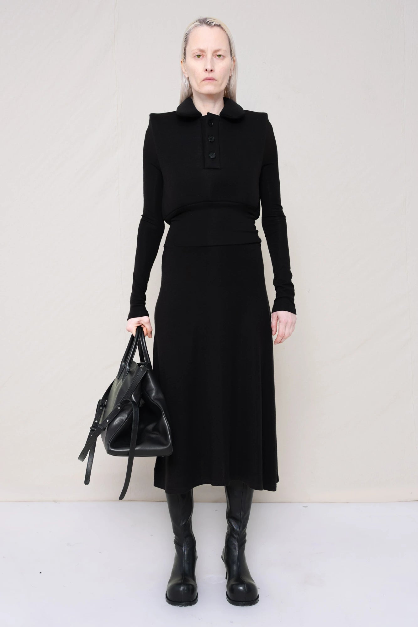 PERSON-WEARING-BLACK-LONG-SLEEVE-FOAMY-POLO-DRESS-WITH-BLACK-DOUBLE-HEELED-BOOTS-HOLDING-BLACK-COWHIDE-A-LINE-SHOPPER-FRONT-VIEW