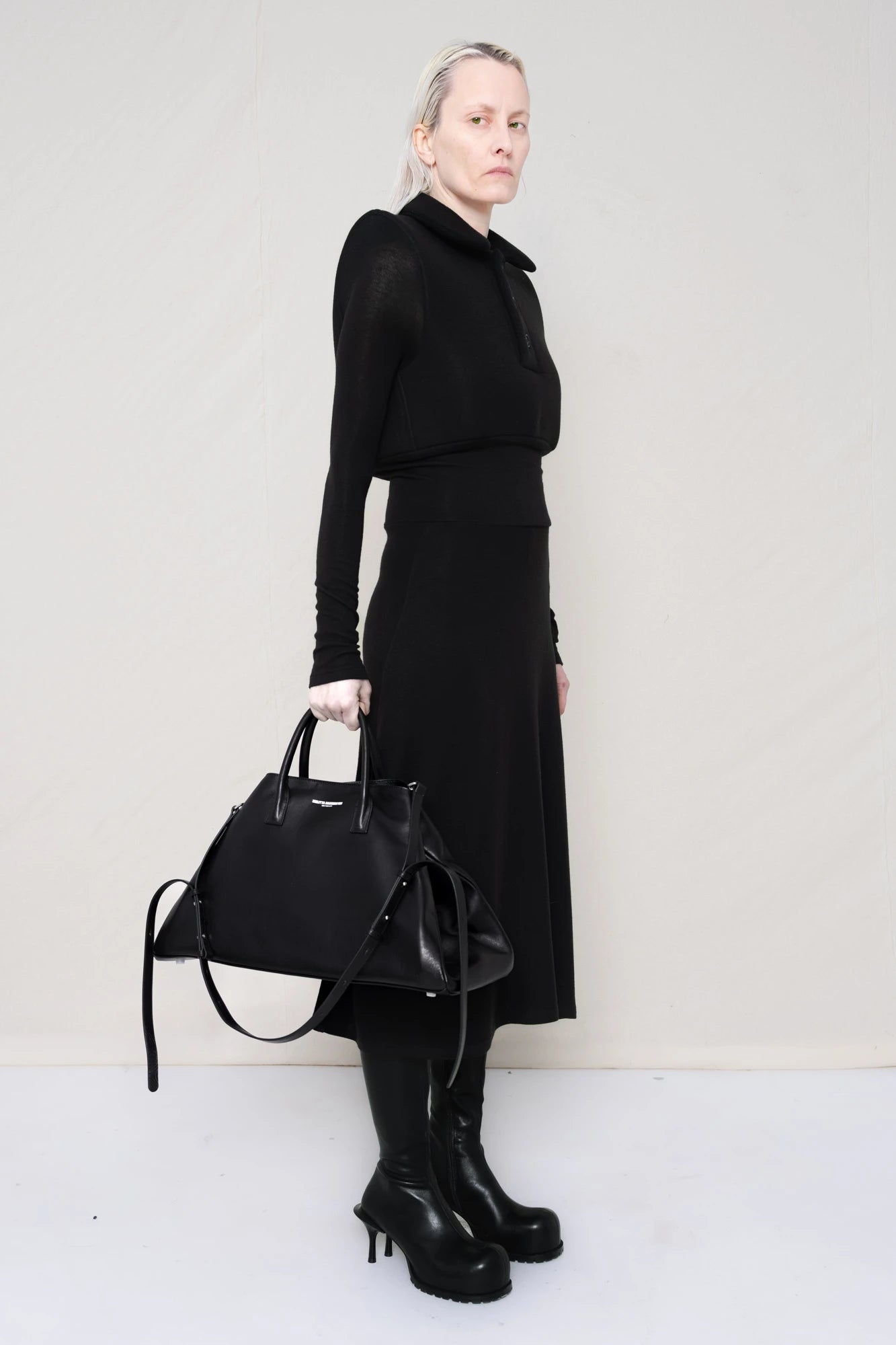 PERSON-WEARING-BLACK-LONG-SLEEVE-FOAMY-POLO-DRESS-WITH-BLACK-DOUBLE-HEELED-BOOTS-HOLDING-BLACK-COWHIDE-A-LINE-SHOPPER-THREE-QUARTER-VIEW