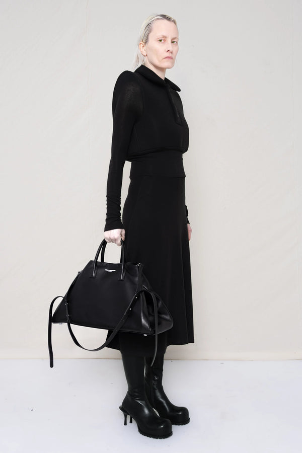 PERSON-WEARING-BLACK-LONG-SLEEVE-FOAMY-POLO-DRESS-WITH-BLACK-DOUBLE-HEELED-BOOTS-HOLDING-BLACK-COWHIDE-A-LINE-SHOPPER-THREE-QUARTER-VIEW
