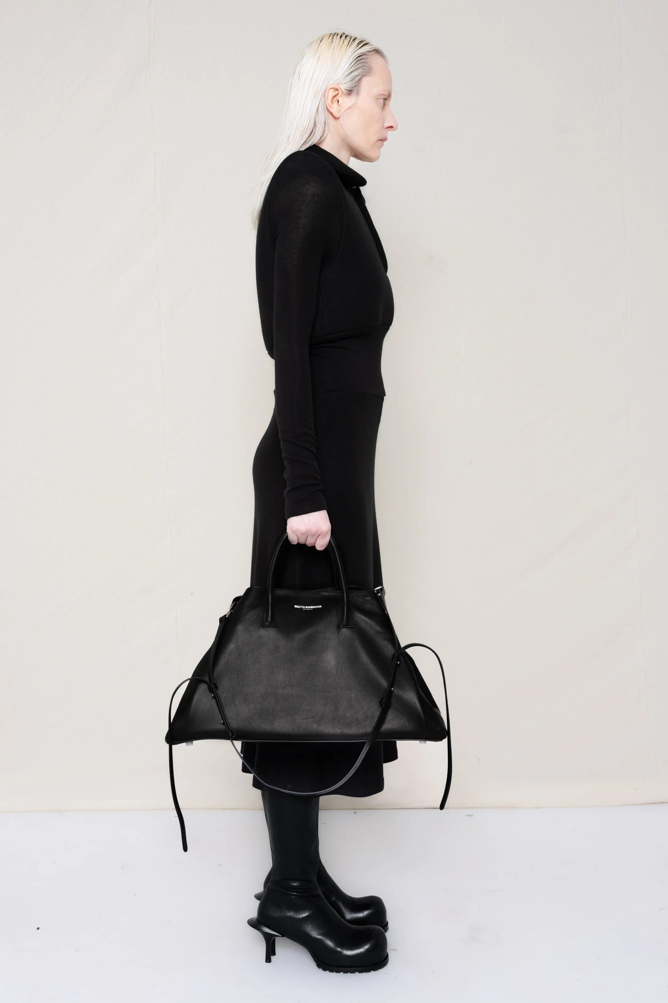 PERSON-WEARING-BLACK-LONG-SLEEVE-FOAMY-POLO-DRESS-WITH-BLACK-DOUBLE-HEELED-BOOTS-HOLDING-BLACK-COWHIDE-A-LINE-SHOPPER-SIDE-VIEW