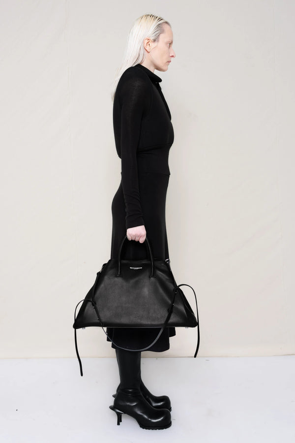 PERSON-WEARING-BLACK-LONG-SLEEVE-FOAMY-POLO-DRESS-WITH-BLACK-DOUBLE-HEELED-BOOTS-HOLDING-BLACK-COWHIDE-A-LINE-SHOPPER-SIDE-VIEW