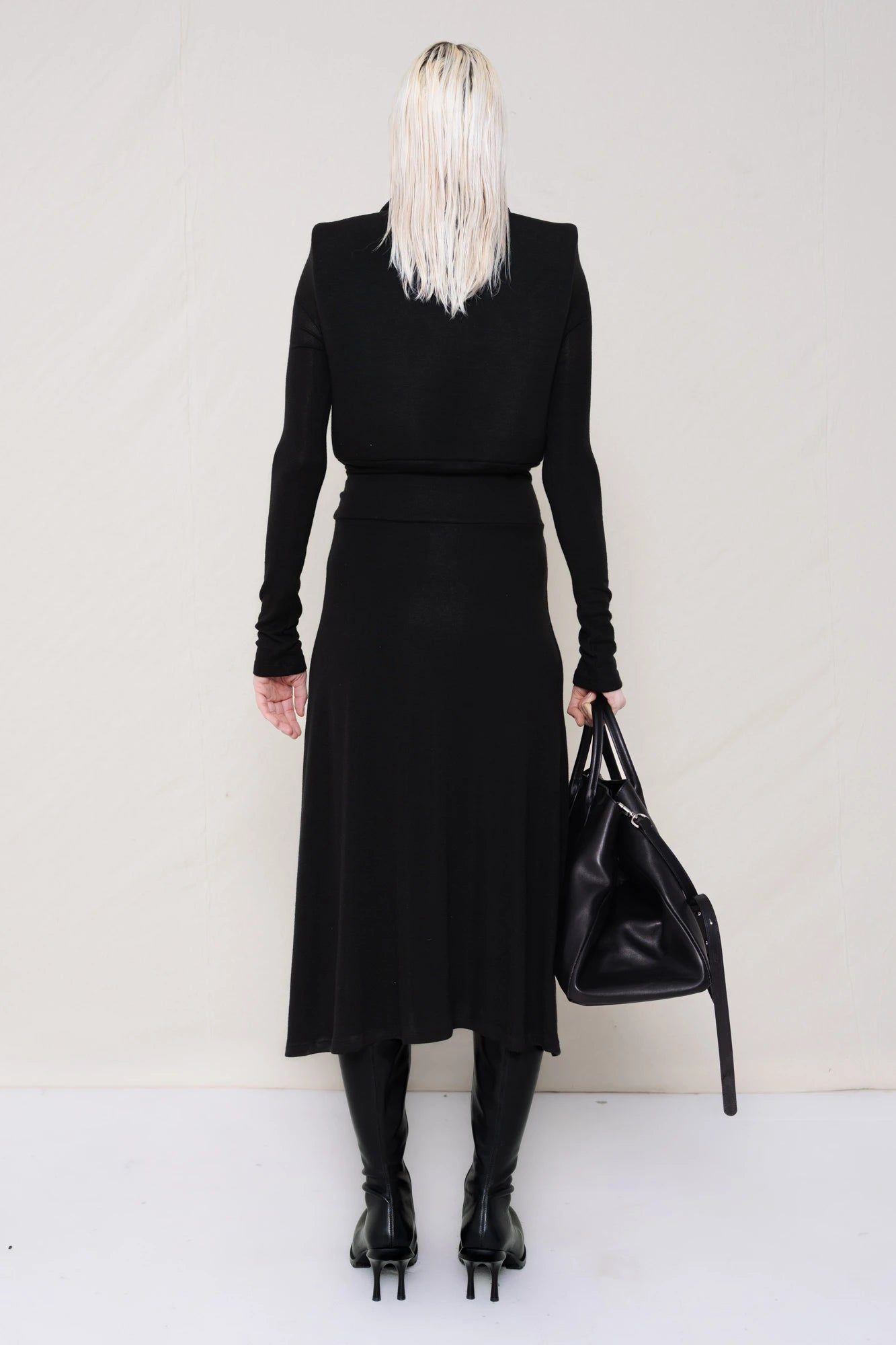 PERSON-WEARING-BLACK-LONG-SLEEVE-FOAMY-POLO-DRESS-WITH-BLACK-DOUBLE-HEELED-BOOTS-HOLDING-BLACK-COWHIDE-A-LINE-SHOPPER-BACK-VIEW