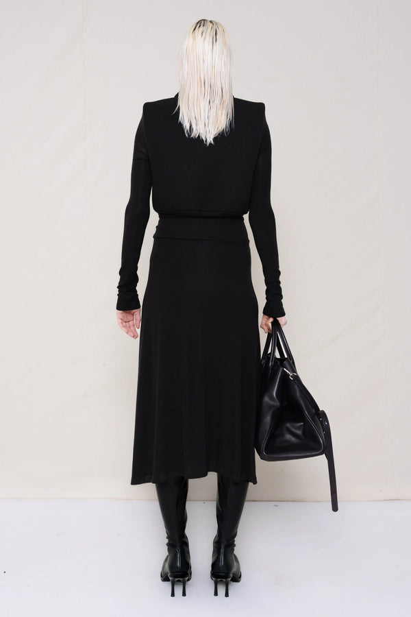 PERSON-WEARING-BLACK-LONG-SLEEVE-FOAMY-POLO-DRESS-WITH-BLACK-DOUBLE-HEELED-BOOTS-HOLDING-BLACK-COWHIDE-A-LINE-SHOPPER-BACK-VIEW