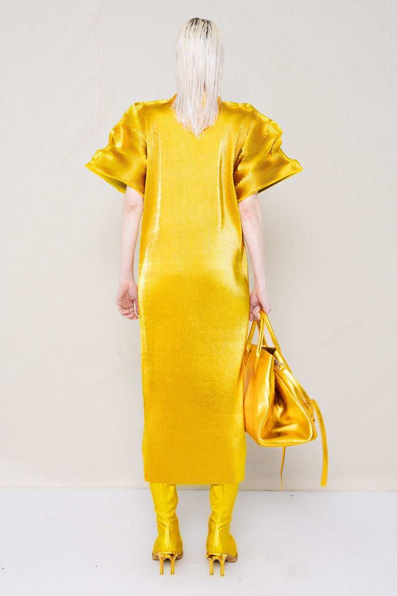 PERSON-WEARING-GOLD-PLEAT-MALLEABLE-SHOULDER-DRESS-WITH-MATCHING-GOLD-COWHIDE-DOUBLE-HEELED-BOOTS-HOLDING-GOLD-A-LINE-SHOPPER-BAG-BACK-VIEW