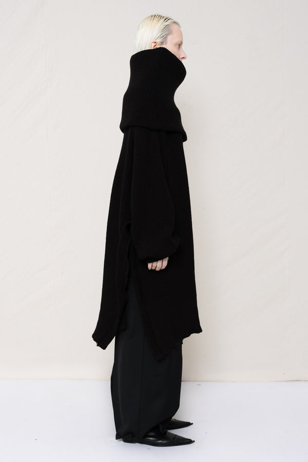 PERSON-WITH-GREEN-EYES-WEARING-BLACK-OVERSIZE-LONG-ROLL-NECK-OVER-SHOULDERS-SWEATER-WITH-BLACK-LONG-TAILORED-TROUSERS-AND-BLACK-COWHIDE-BOOTS-SIDE-VIEW