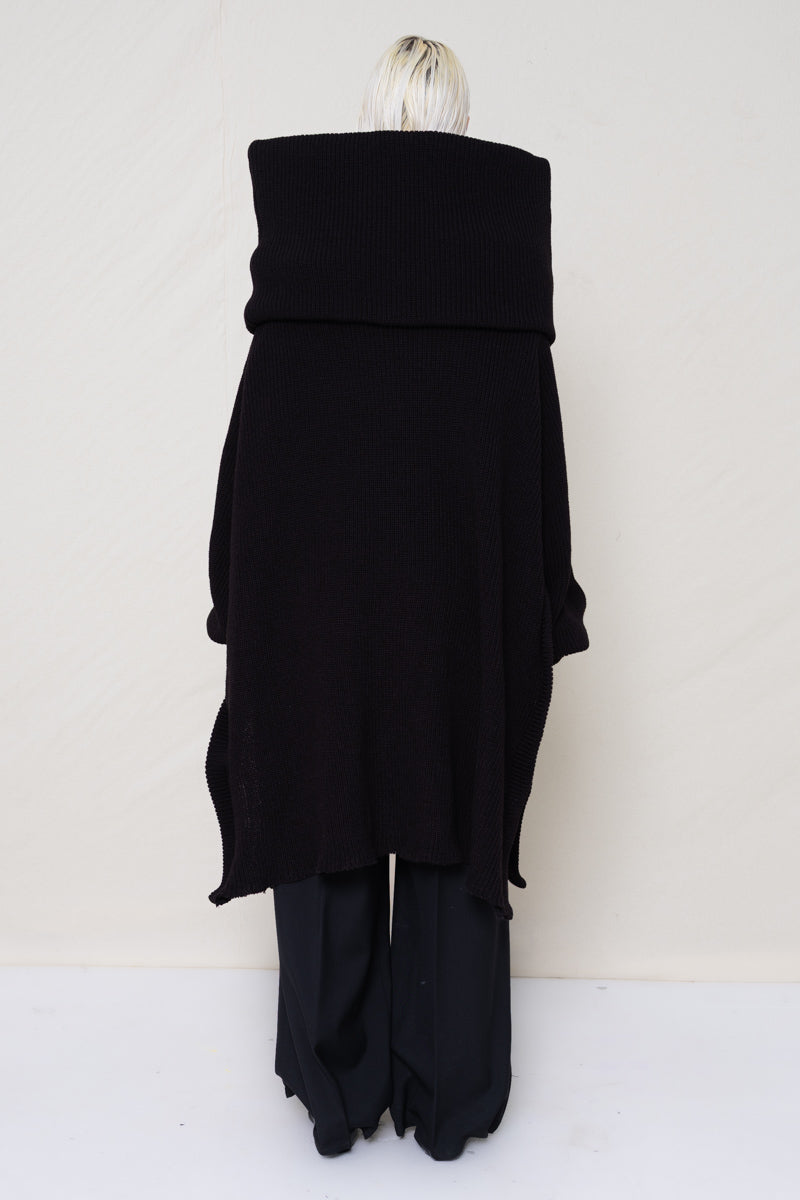 PERSON-WITH-GREEN-EYES-WEARING-BLACK-OVERSIZE-LONG-ROLL-NECK-OVER-SHOULDERS-SWEATER-WITH-BLACK-LONG-TAILORED-TROUSERS-AND-BLACK-COWHIDE-BOOTS-HOLDING-BLACK-A-LINE-SHOPPER-BACK-VIEW