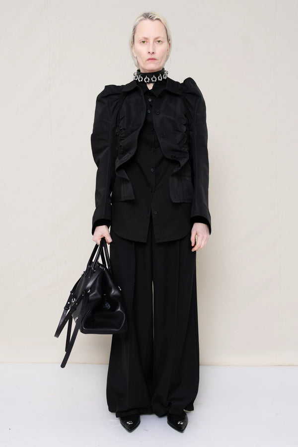 PERSON-WEARING-BLACK-GATHERING-SHIRT-OVER-BLACK-SHIRT-THROW-OVER-WITH-BLACK-LONG-TAILORED-TROUSERS-AND-BLACK-COWHIDE-FRONT-PIERCED-BOOTS-HOLDING-BLACK-A-LINE-SHOPPER-WITH-PIERCING-DETAILS-AND-WEAR-ACCESOIRES-WITH-ALLOVER-PIERCED-NECKLACE-FRONT-VIEW