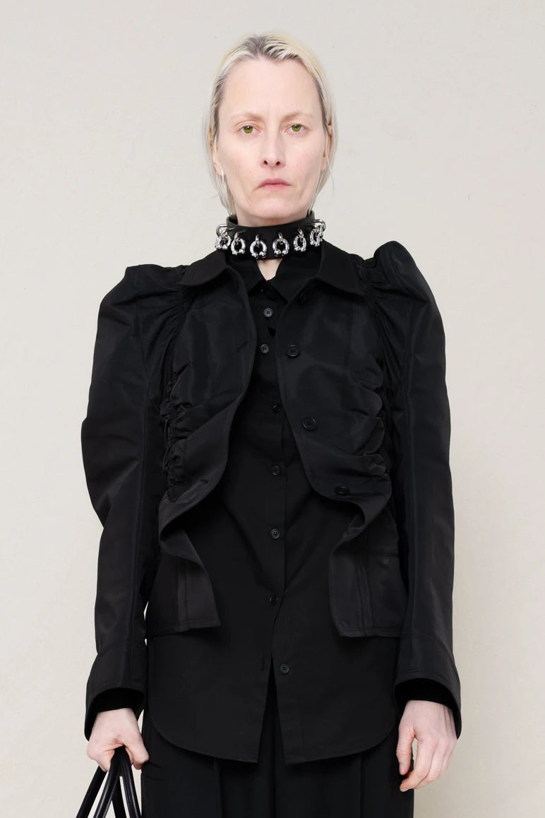 PERSON-WEARING-BLACK-GATHERING-SHIRT-OVER-BLACK-SHIRT-THROW-OVER-WITH-BLACK-LONG-TAILORED-TROUSERS-AND-BLACK-COWHIDE-FRONT-PIERCED-BOOTS-HOLDING-BLACK-A-LINE-SHOPPER-WITH-PIERCING-DETAILS-AND-WEAR-ACCESOIRES-WITH-ALLOVER-PIERCED-NECKLACE-FRONT-VIEW