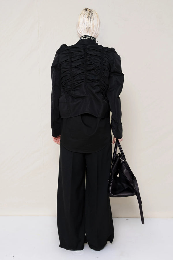 PERSON-WEARING-BLACK-GATHERING-SHIRT-OVER-BLACK-SHIRT-THROW-OVER-WITH-BLACK-LONG-TAILORED-TROUSERS-AND-BLACK-COWHIDE-FRONT-PIERCED-BOOTS-HOLDING-BLACK-A-LINE-SHOPPER-WITH-PIERCING-DETAILS-AND-WEAR-ACCESOIRES-WITH-ALLOVER-PIERCED-NECKLACE-BACK-VIEW