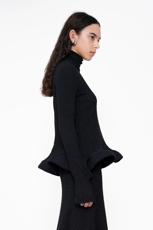 female-wearing-tight-black-longsleeve-turtleneck-top-with-wavy-hem-and-hole-in-sleeve-detail-on-white-background-close-up-torso-side