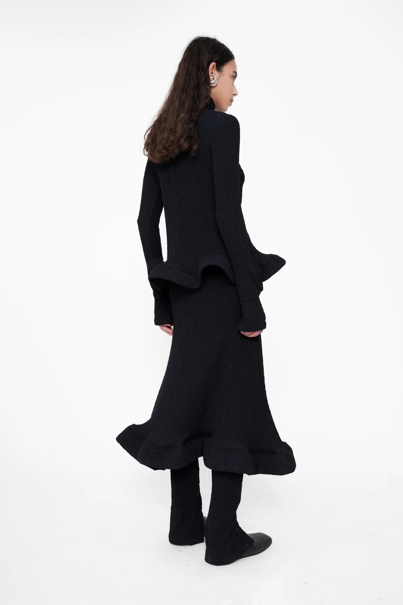 female-wearing-tight-black-longsleeve-turtleneck-top-with-wavy-hem-and-hole-in-sleeve-detail-on-white-background-full-body-back-side