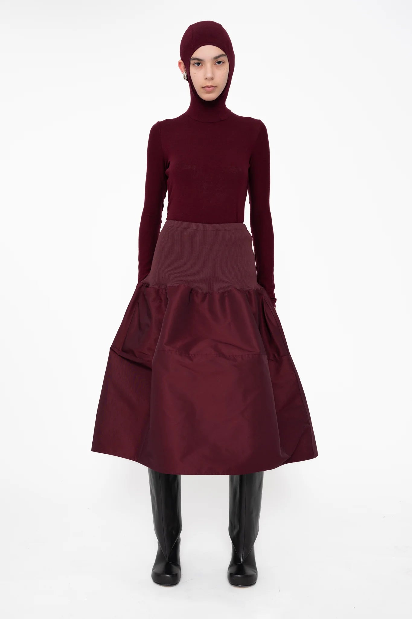female-wearing-bordeaux-bomber-skirt-with-bordeaux-balaclava-top-with-ear-holes-and-black-double-heel-boots-on-white-background-full-body-front