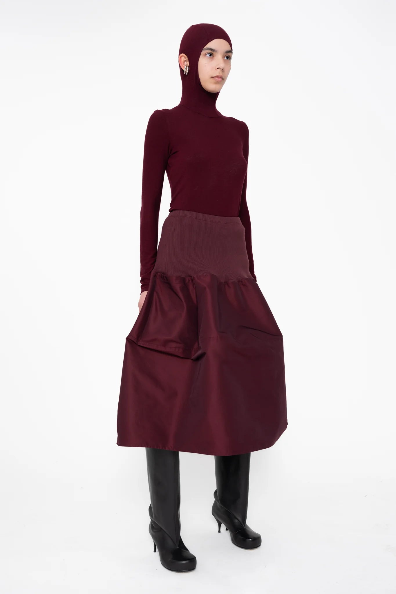 female-wearing-bordeaux-bomber-skirt-with-bordeaux-balaclava-top-with-ear-holes-and-black-double-heel-boots-on-white-background-full-body-three-quarter