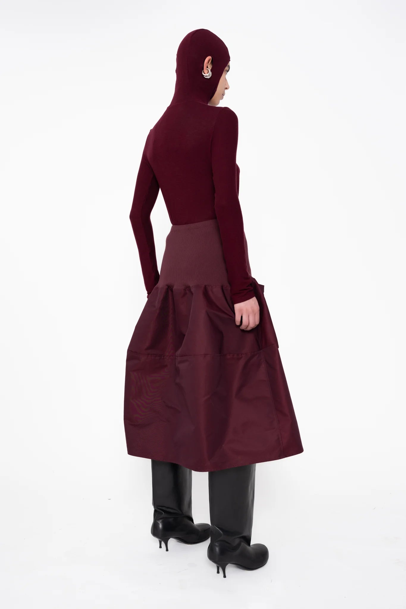 female-wearing-bordeaux-bomber-skirt-with-bordeaux-balaclava-top-with-ear-holes-and-black-double-heel-boots-on-white-background-full-body-back-side