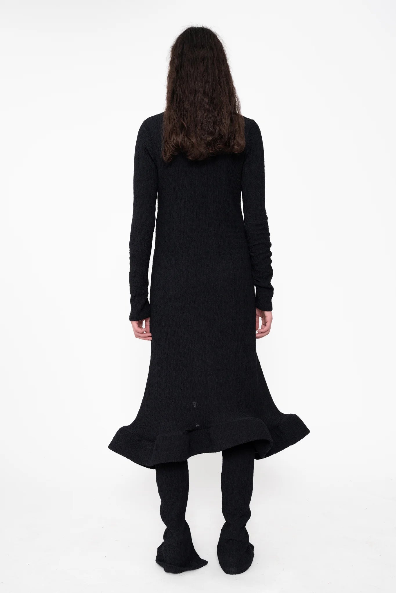 female-wearing-black-longsleeve-midi-dress-with-wavy-hem-and-button-closure-on-white-background-full-body-back